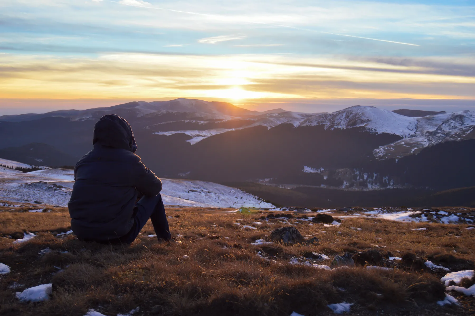 A person sitting on a mountainside at sunset, looking out over the ridges